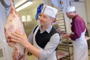 A butcher holding and smiling at a piece of meat