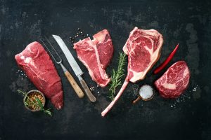 4 cuts of wholesale meat laid out with knives and peppers around it